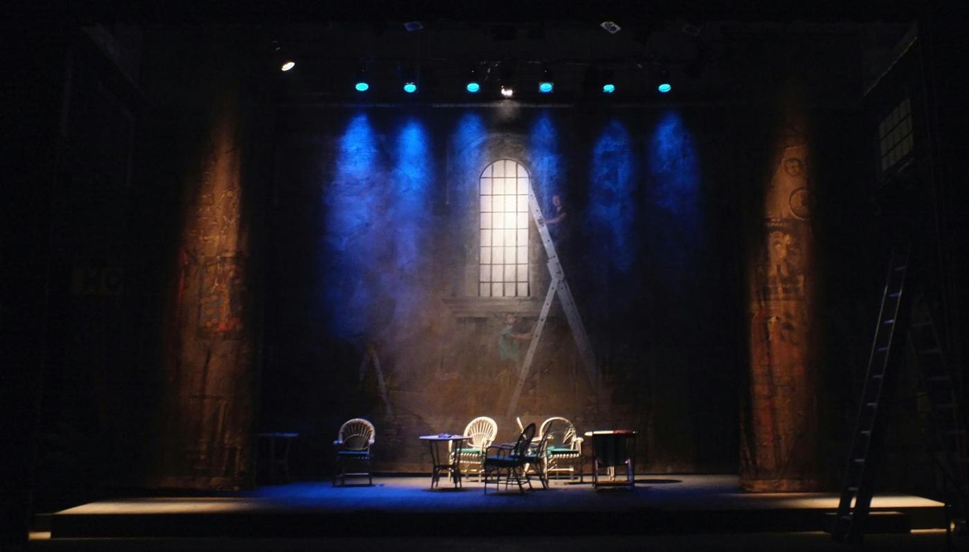 A bare stage lit blue, with a table and two chairs